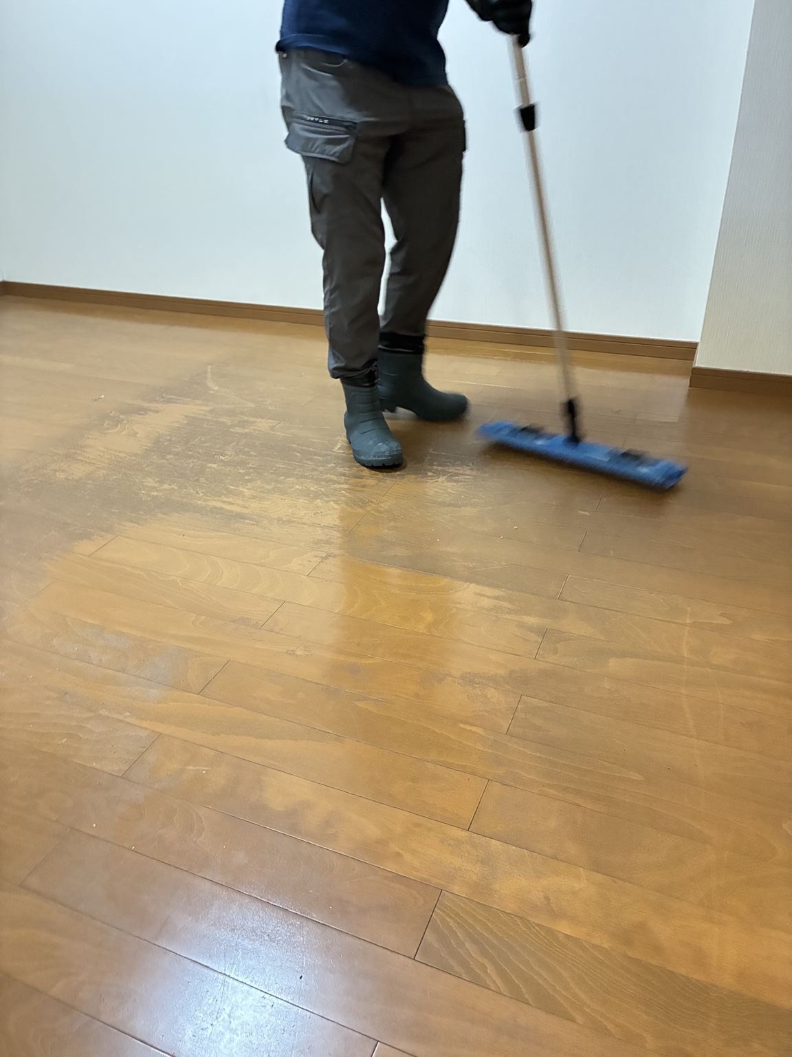 剥離作業前の木目調の床を青いダスターモップで除塵する作業員